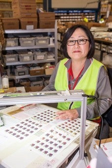 Esther,  Australia Post's philatelic postmarking officer standing in front of a postmarking machine smiling at camera Esther,  Australia Post's philatelic postmarking officer standing in front of a postmarking machine smiling at camera